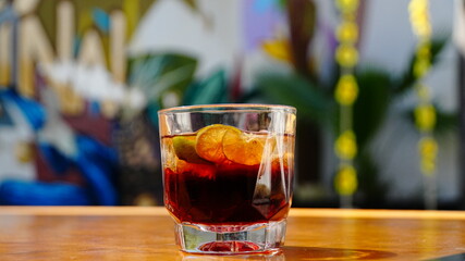 vaso corto con bebida oscura y rodajas de limón. Fondo tropical y ambiente relajado.