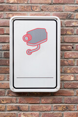 Surveillance camera sign on a red brick wall. Information plate indicating video monitoring (CCTV) area. Concept of security, surveillance, and property protection.