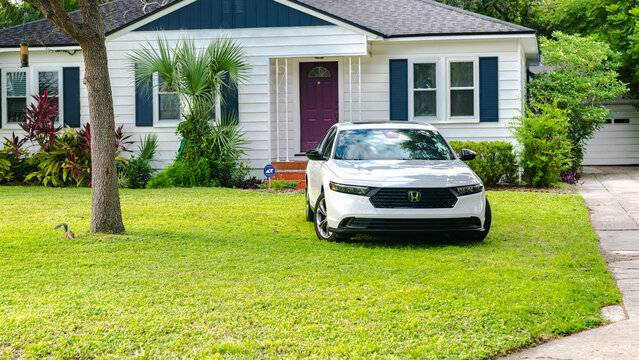Clean white car parked on grass in front of charming white house with purple door