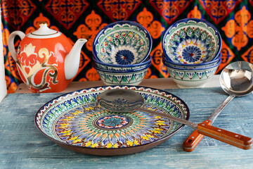 Handcrafted ceramic bowls and platter with a red floral teapot in ethnic Central Asian style.