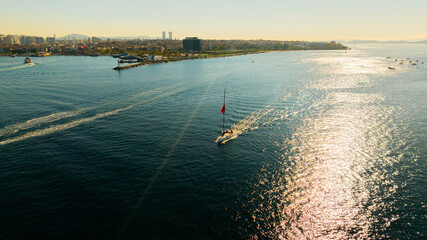 Aerial view Sailboat With Turkish Flag Cruising The Open Sea Under Clear Sky. A lone sailboat glides across calm blue waters, its bright Turkish flag fluttering from the mast. The scene conveys travel