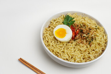 A bowl of instant noodles topped with half boiled egg, minced meat, and chili garnish, served with chopsticks on white background. Clean minimalist Asian food concept.