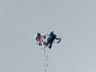 Aerial top-down view of mother and daughter making snow angels in a pristine white snowfield in Estonia.