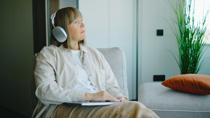 Elderly woman enjoying quiet moments while listening to music and reflecting in a cozy living room...