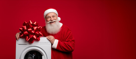 cheerful Santa Claus posing next to washing machine with shiny bow, red background studio shot, concept of Christmas discounts and modern appliance gifts, bright joyful atmosphere
