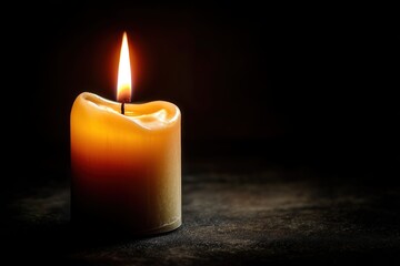 A single, partially melted yellow candle with a tall flame on a dark surface, casting a soft glow in a black background.