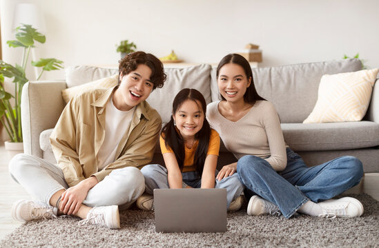 A happy family of three sits together on a soft rug, watching a movie on a laptop in their comfortable living room. The atmosphere feels warm and inviting.