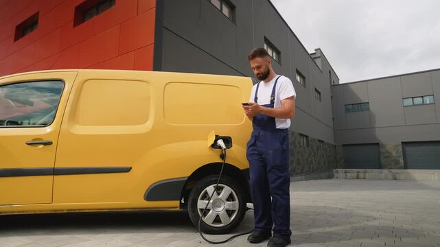 Delivery man charging electric van and using smartphone