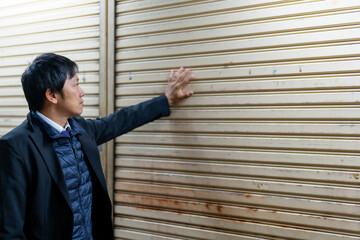 老朽化したシャッターを点検するスーツの男性