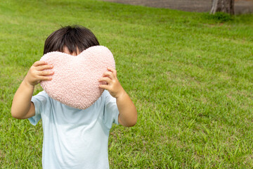 ハートのクッションを持って草原に立つ男の子（2歳、日本人、顔無し）