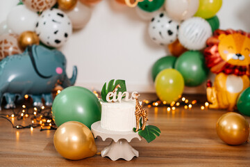 Minimal white birthday cake with giraffe figure, tropical leaves, and “eins” topper.