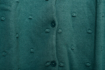 Close-up of green knitted sweater with buttons, textile texture background.