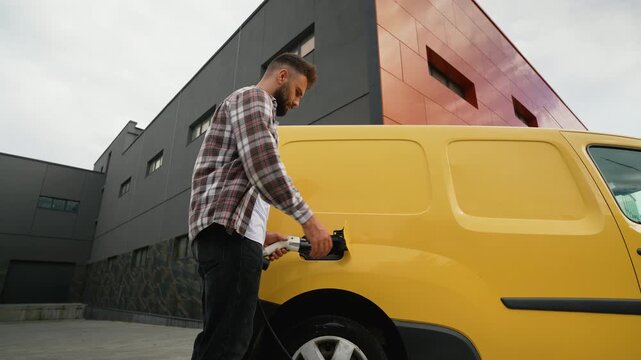 Male driver unplugging electric van from charging station