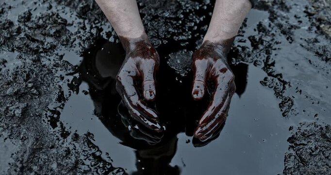 His hands are stained with crude oil against the background of spilled petroleum products.  crisis of the oil industry.  economic downturn. concept of the oil industry, production, and oil production.