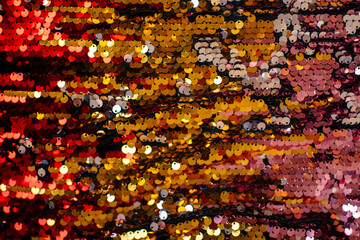 Shiny gold and red sequin background, festive glitter texture close-up.