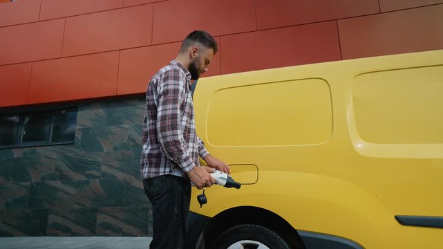 Delivery man unplugging charging cable from electric van