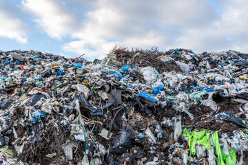 Plastic waste pile in a landfill near a city under a cloudy sky