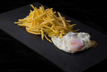 Huevo frito con patatas fristas sobre tabla de pizarra con fondo oscuro
