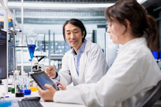 Joyous lab scientists using tablet to evaluate genetic markers associated with disease risk. Smiling senior researcher and colleague study DNA strand mapping with genomics analysis app on device - Powered by Adobe