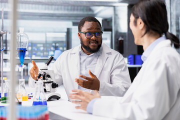 Multiethnic team of microbiologists in laboratory inspecting specimen slide for microscopy study using optical device. Multiracial lab coworkers reviewing cytology slide for clinical testing procedure