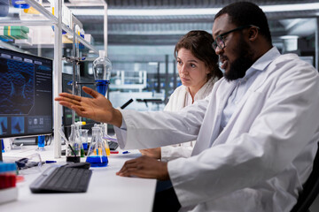 Diagnostic laboratory manager and woman using computer program for DNA data analysis. Research facility team leader and employee using bioinformatics genomics software on PC in modern lab
