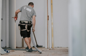 A young man vacuums the floor with a construction vacuum cleaner.