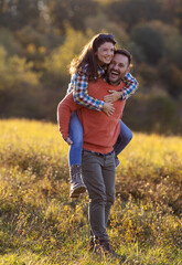 Husband and wife piggyback in field