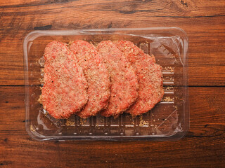 Lamb uncooked steak coated in Arabic Harissa style herbs and spices in plastic tray on wooden table. Red minced meat. Fine butcher style burgers ready for cooking.