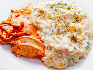 Portion of potato and corn salad and red hot slices of Cajun chicken fillet on a white plate. Simple tasty dinner.