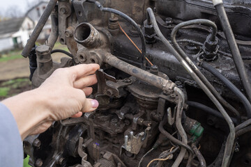 Detailed view of human hand examining car engine elements during maintenance in outdoor repair yard. Perfect for automotive, industry, and mechanic-related themes.