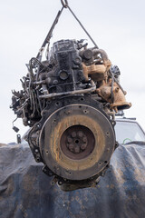 Worn automobile engine hanging on a crane for maintenance