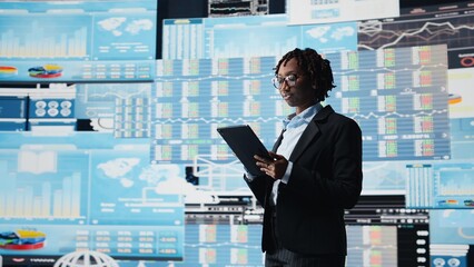 Manager using tablet to compare company metrics on digital videowall before making decisions....