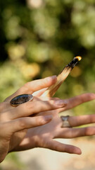 A close-up of a woman's hands holding a smoking palo santo stick while performing a magical ritual...