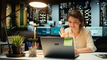 Businesswoman joins an online meeting at night in corporate office, maintaining eye contact with...