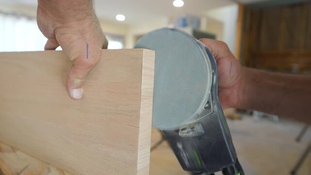 Worker sanding the edge of a wooden board using a handheld power sander. Smoothing process, showing the craftsman hands guiding the tool along the wood grain.