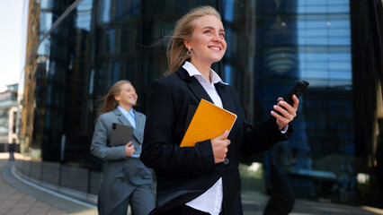 Young professionals walking confidently outside a modern office building with mobile devices