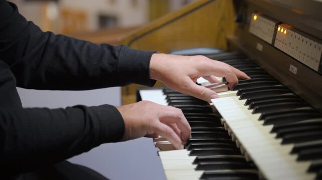 Musician plays an organ inside a church or concert hall. The performer hands actively moving across multiple manuals keyboards, suggesting live performance. 