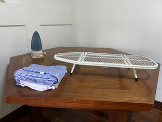 an iron, a metal ironing board, and clothes, placed on a wooden table