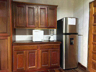 A blender placed to the right of a bread maker, above a low kitchen cabinet, and a refrigerator and also a tall kitchen cabinet.
