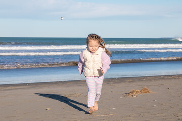 Cute little girl running barefoot along the beach on a sunny day. Happy child enjoying outdoor play
