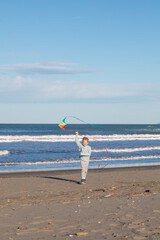 Joyful young boy running along the beach and flying a colorful kite. Fun outdoor activity for kids