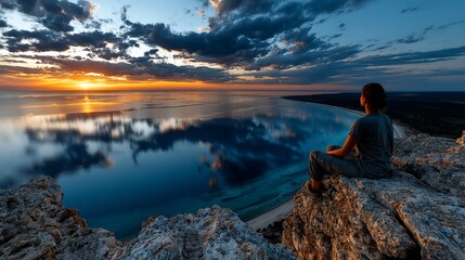 Man sitting on rocks watching lake sunset reflection with dramatic clouds for emotional travel adventure and inspirational moment photography