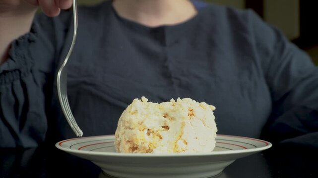 A plump woman picks up a piece of cake on a plate with a fork. Low angle, home interior, soft light. A plump woman with a headless appearance eats a piece of cake.