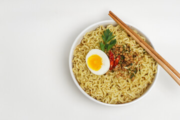 A bowl of instant noodles with half boiled egg, minced meat, and red chili, served with chopsticks on white background. Minimalist top view of Asian comfort food.