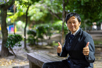 夜の公園でグッドサインをするビジネスマン