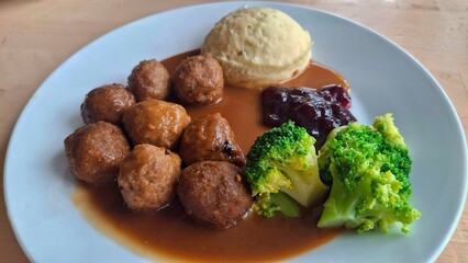 Appetizing plate of IKEA-style Swedish meatballs with gravy, creamy mashed potatoes, and steamed broccoli. Captured in natural light, highlighting the warm and cozy atmosphere of homemade cooking.

