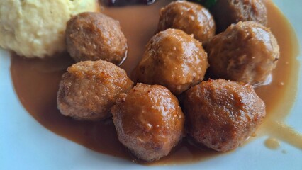 Swedish meatballs with creamy mashed potatoes, rich brown gravy, lingonberry sauce, and broccoli served on a white plate.