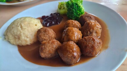 Close-up of delicious Swedish meatballs covered in brown gravy, paired with mashed potatoes and broccoli. Classic Nordic comfort food known for its savory flavor and homestyle presentation.
