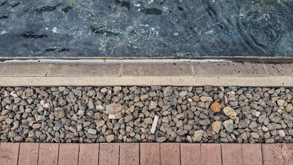 Minimalist outdoor detail featuring a section of water beside a stone border and wooden decking. 