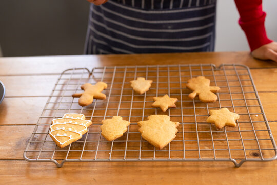 Cooling rack holding gingerbread men, star, tree cookies on kitchen counter, baker hands decorating